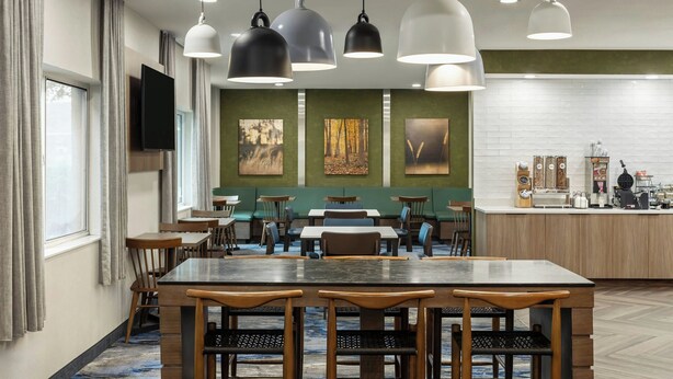 A modern dining area with multiple tables and chairs, pendant lighting, artwork on the walls, and a kitchen counter with appliances.