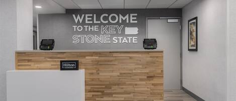 A reception desk with a 'Welcome to the Key Stone State' sign, a 'Hilton Honors' badge, and a wooden panel design.