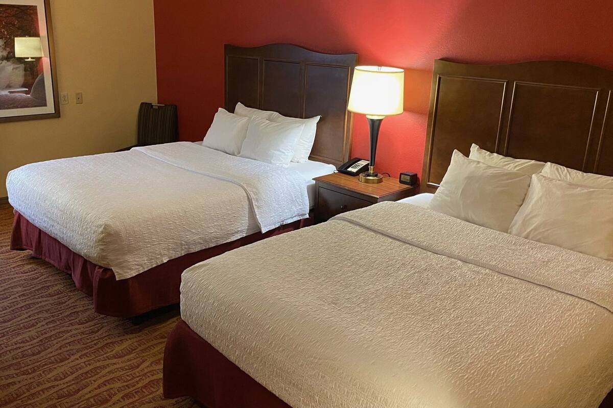 Two double beds with white linens, a nightstand with a lamp, and a red wall.