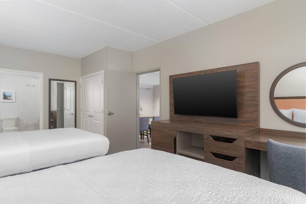 A hotel room with two beds, a flat-screen TV, a mirror, and a desk with drawers.