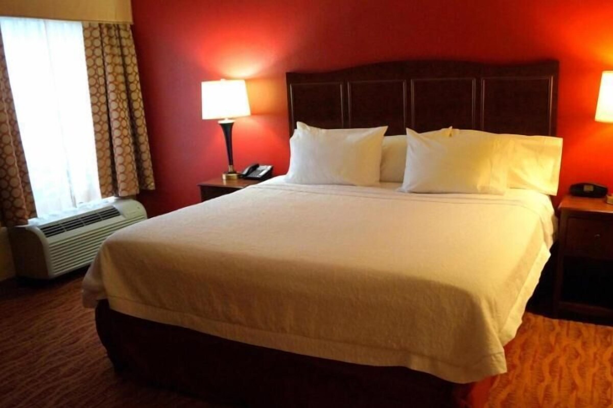A hotel room with a large bed, a bedside lamp, a telephone, and a window with curtains.