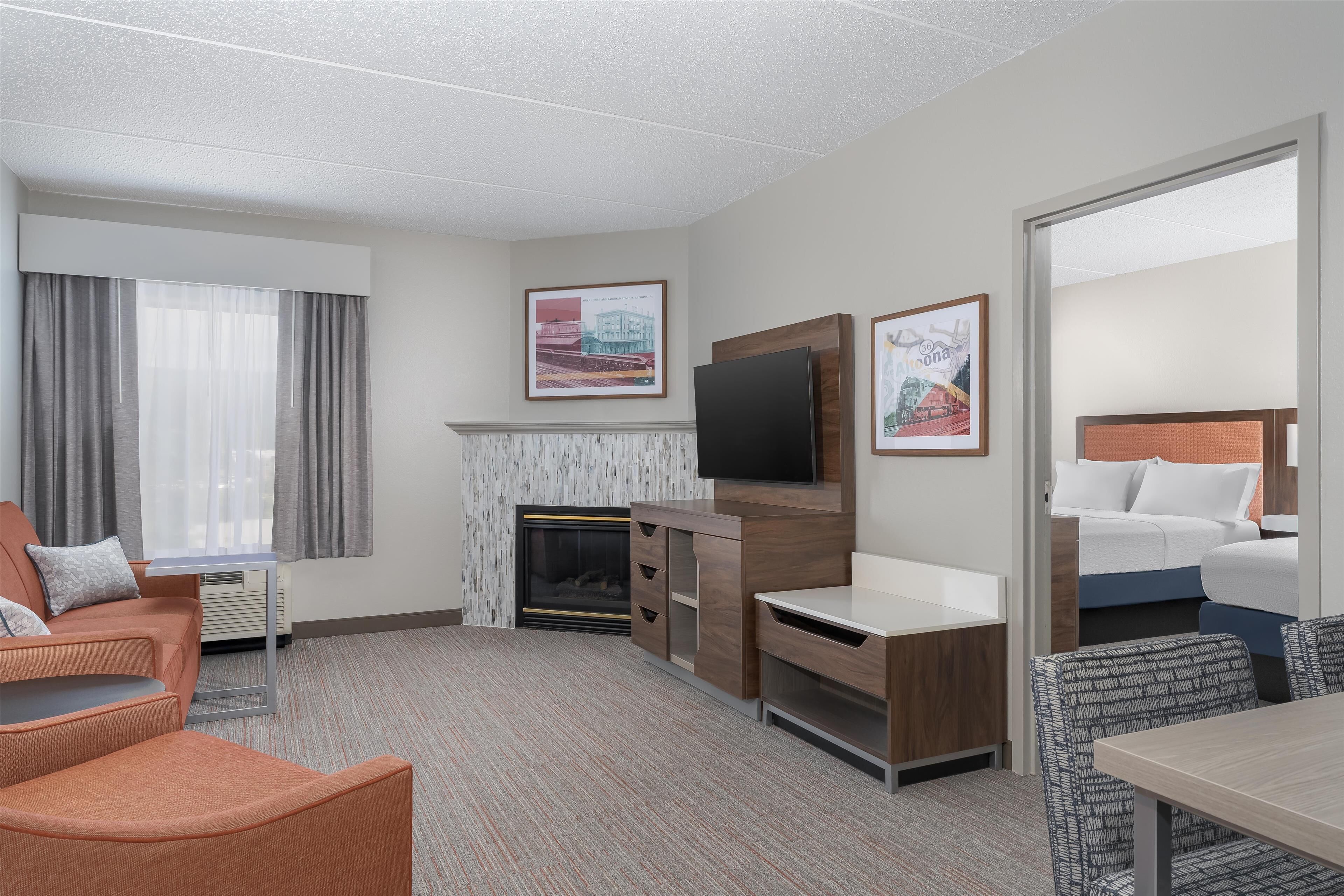 A hotel room with a fireplace, a TV mounted on the wall, a bed, and a seating area with a table and chairs.