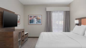 A hotel room with a bed, a TV on a wooden dresser, a painting of a waterfall, and a window with curtains.