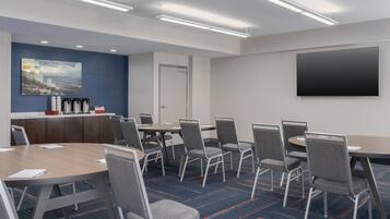 Un salón de conferencias con una gran mesa, varias sillas, un televisor de pantalla plana y una estación de café.