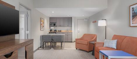 A modern living room with a flat-screen TV, a wooden entertainment unit, a sofa, a coffee table, and a dining area with a table and chairs.