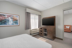 Habitación de hotel con cama, televisor de pantalla plana, mueble de madera, ventana con cortinas y un cuadro en la pared.