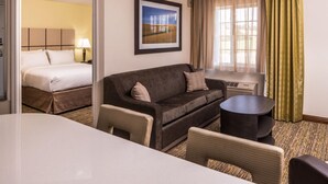 A hotel room with a bed, a sofa, a small table, and a desk. - MainStay Suites Kansas City Overland Park (Overland Park)