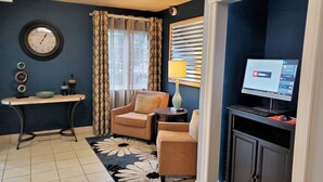 A living room with a sofa, a small table, a lamp, a TV, and a clock on the wall. - MainStay Suites Kansas City Overland Park (Overland Park)