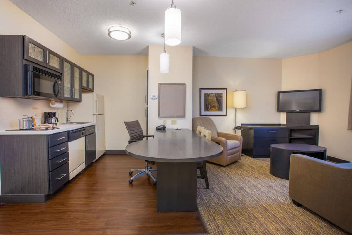A hotel room with a kitchenette, a dining table, a TV, and a sofa.