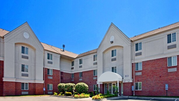 A multi-story hotel with a symmetrical facade, featuring a central entrance with a covered walkway, and a parking area with a handicap parking sign. - MainStay Suites Kansas City Overland Park (Overland Park)