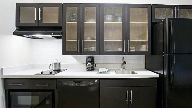 A kitchen with dark cabinets, a black refrigerator, a coffee maker, and a dishwasher. - MainStay Suites Kansas City Overland Park (Overland Park)