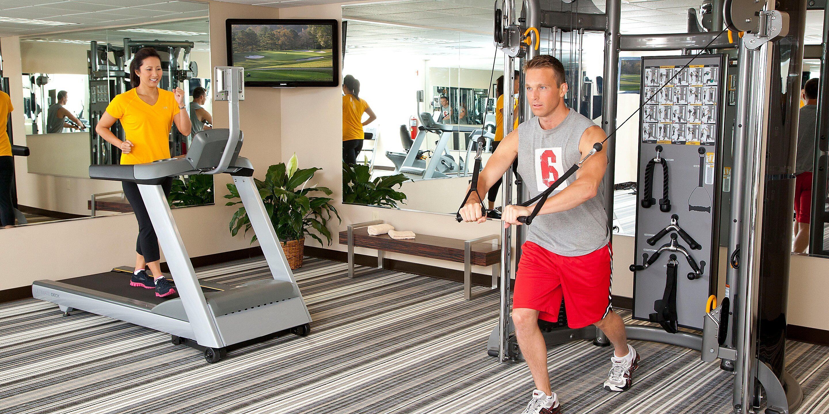 Uma academia com esteiras, aparelhos de exercício e uma tela de televisão.