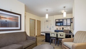A hotel room with a sofa, armchair, dining table, and kitchen area. - MainStay Suites Kansas City Overland Park (Overland Park)