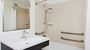 A bathroom with a white sink, a mirror, a shower with a handheld showerhead, and grab bars on the walls. - MainStay Suites Kansas City Overland Park (Overland Park)