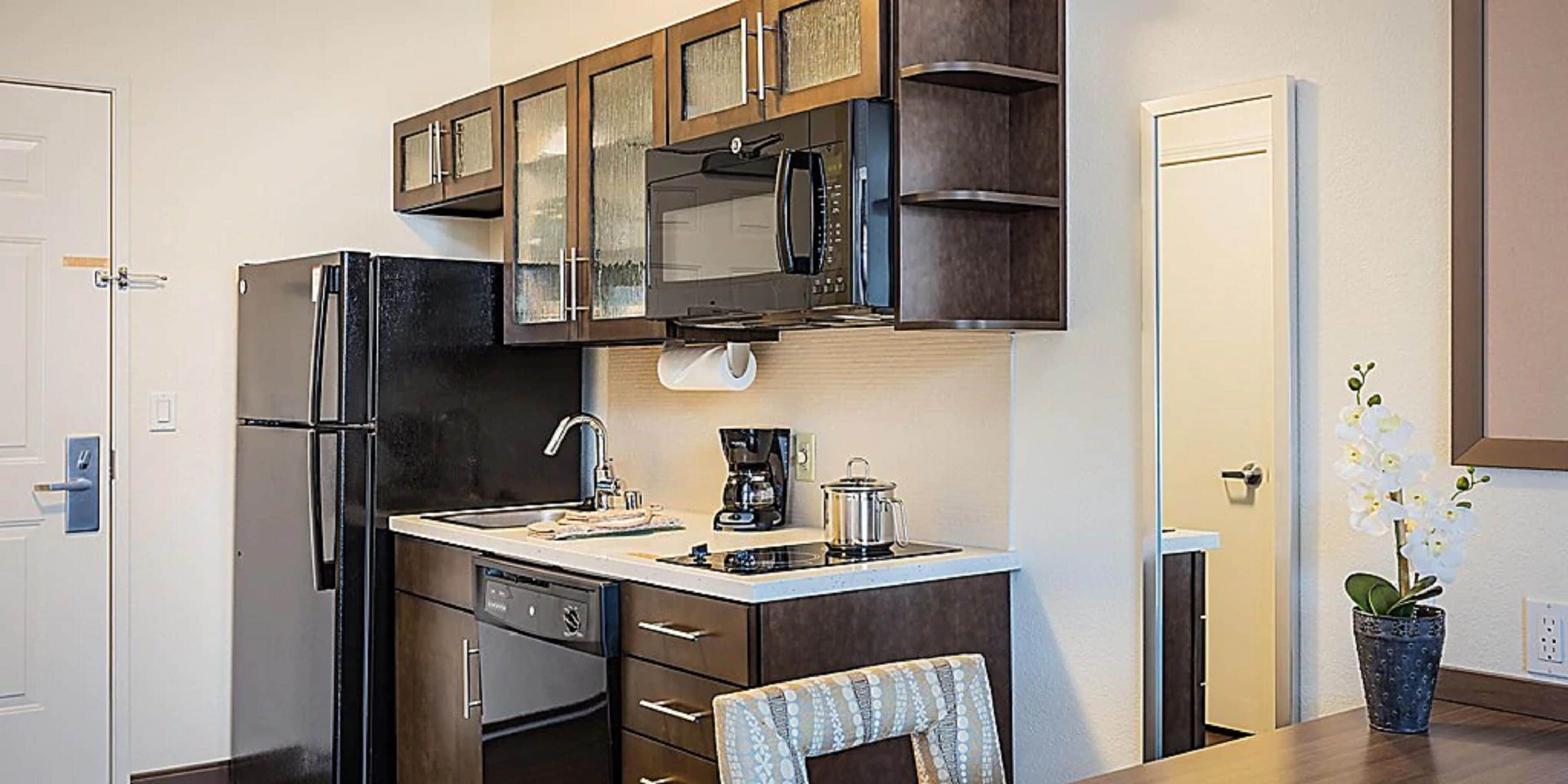 Cocina compacta con refrigerador, microondas y estufa. Cuenta con un lavamanos con grifo, una cafetera y una orquídea en maceta.
