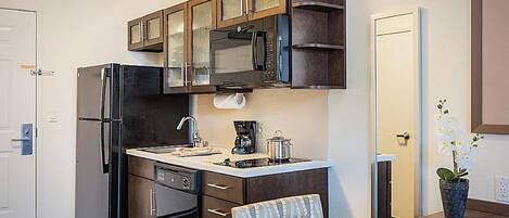 Cocina compacta con refrigerador, microondas y estufa. Cuenta con un lavamanos con grifo, una cafetera y una orquídea en maceta.