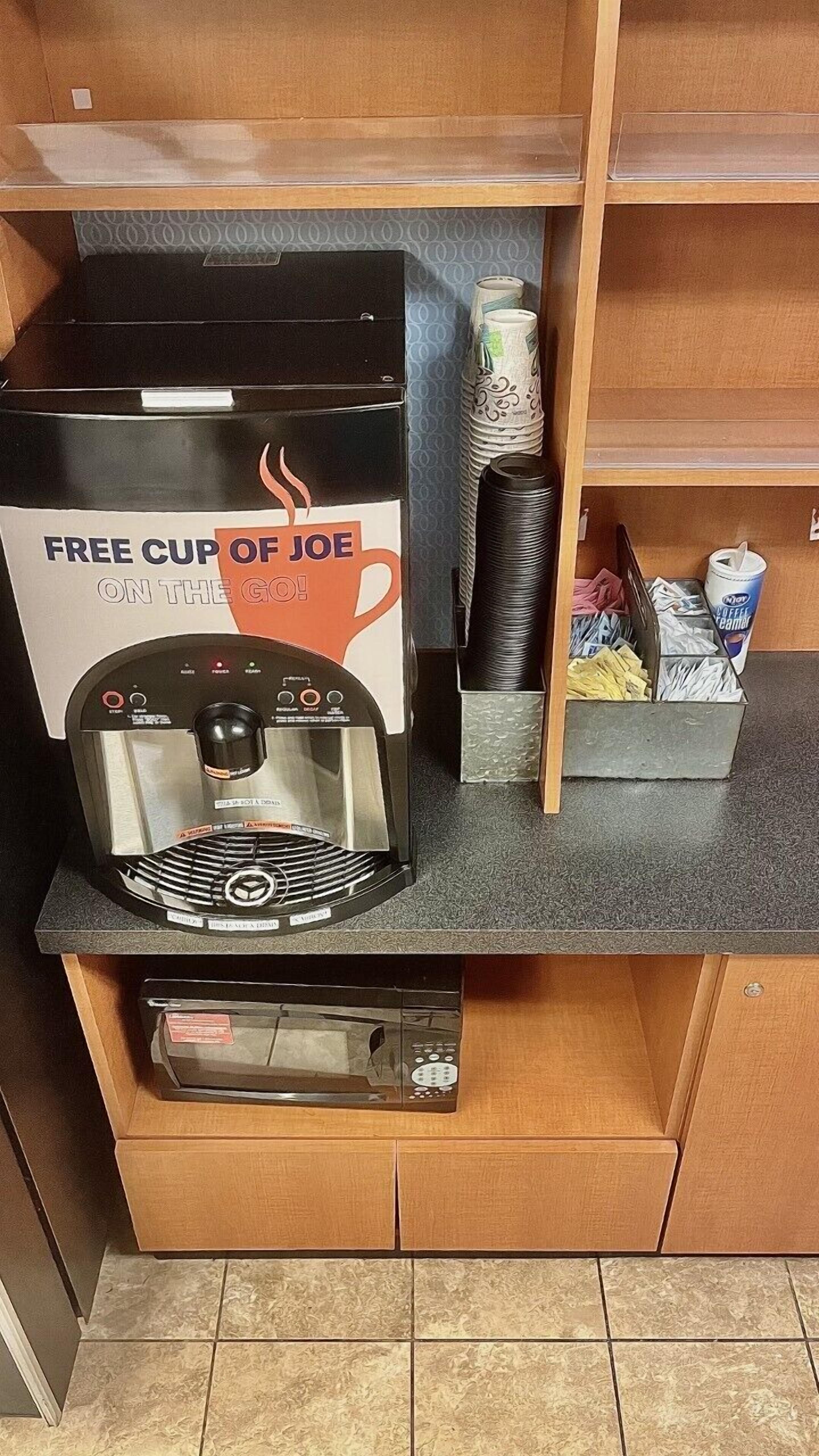 A coffee machine with a sign offering a free cup of joe on the go.