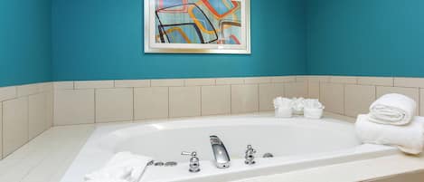 A bathroom with a large bathtub, white towels, and a framed abstract painting on the wall.