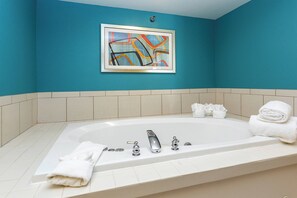 Een badkamer met een groot bad, witte handdoeken en een abstract schilderij in een lijst aan de muur.