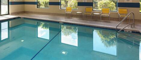 Una piscina interior con agua azul cristalina, sillas amarillas y ventanas amplias que ofrecen vistas al exterior.