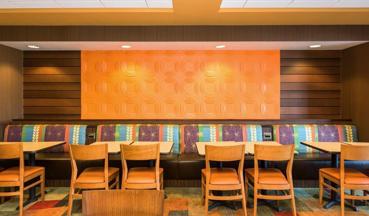 A restaurant with wooden booths and chairs, a patterned wall, and a ceiling with recessed lighting.