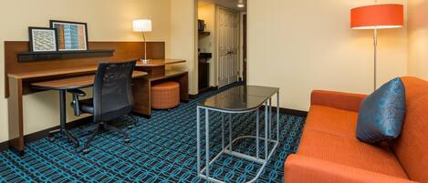 A hotel room with a desk, chair, and orange sofa.