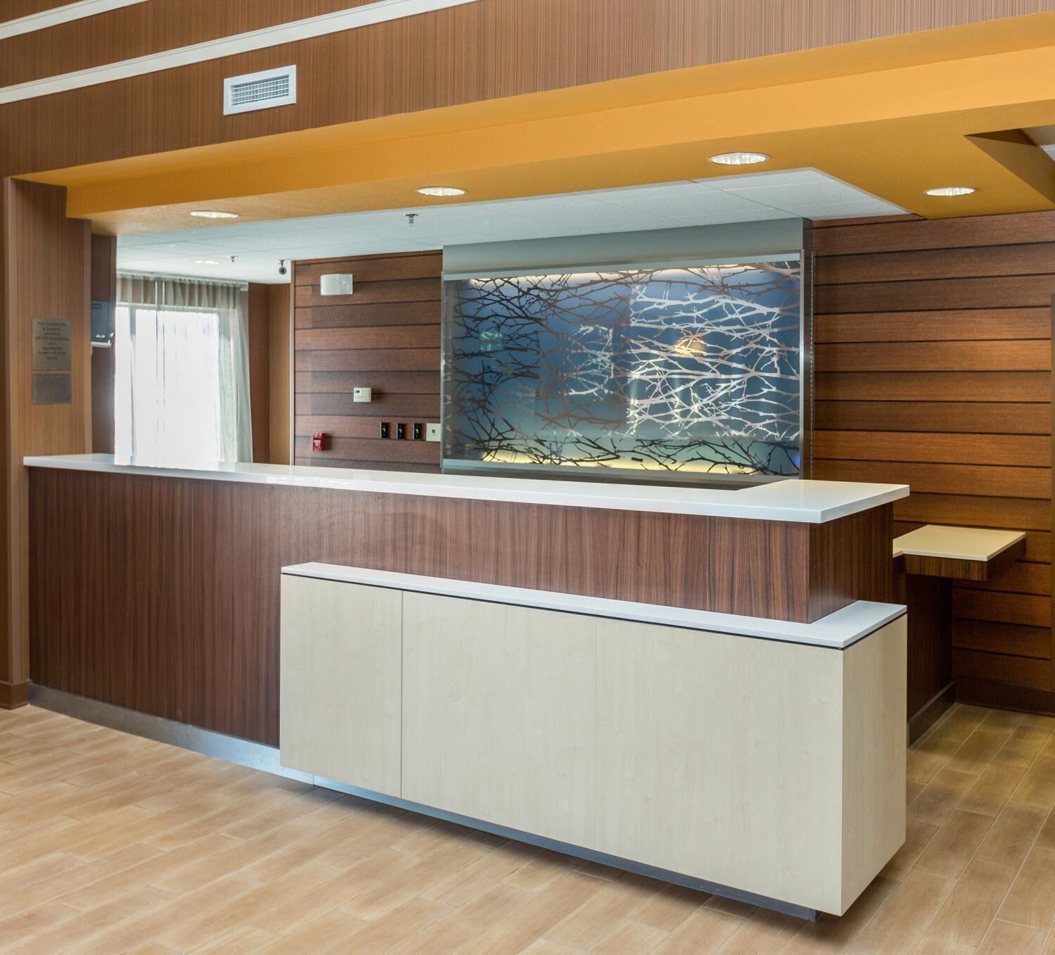 A reception desk with a wooden finish, a glass partition with a tree branch design, and a light-colored floor.