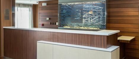 A reception desk with a wooden finish, a glass partition with a tree branch design, and a light-colored floor.