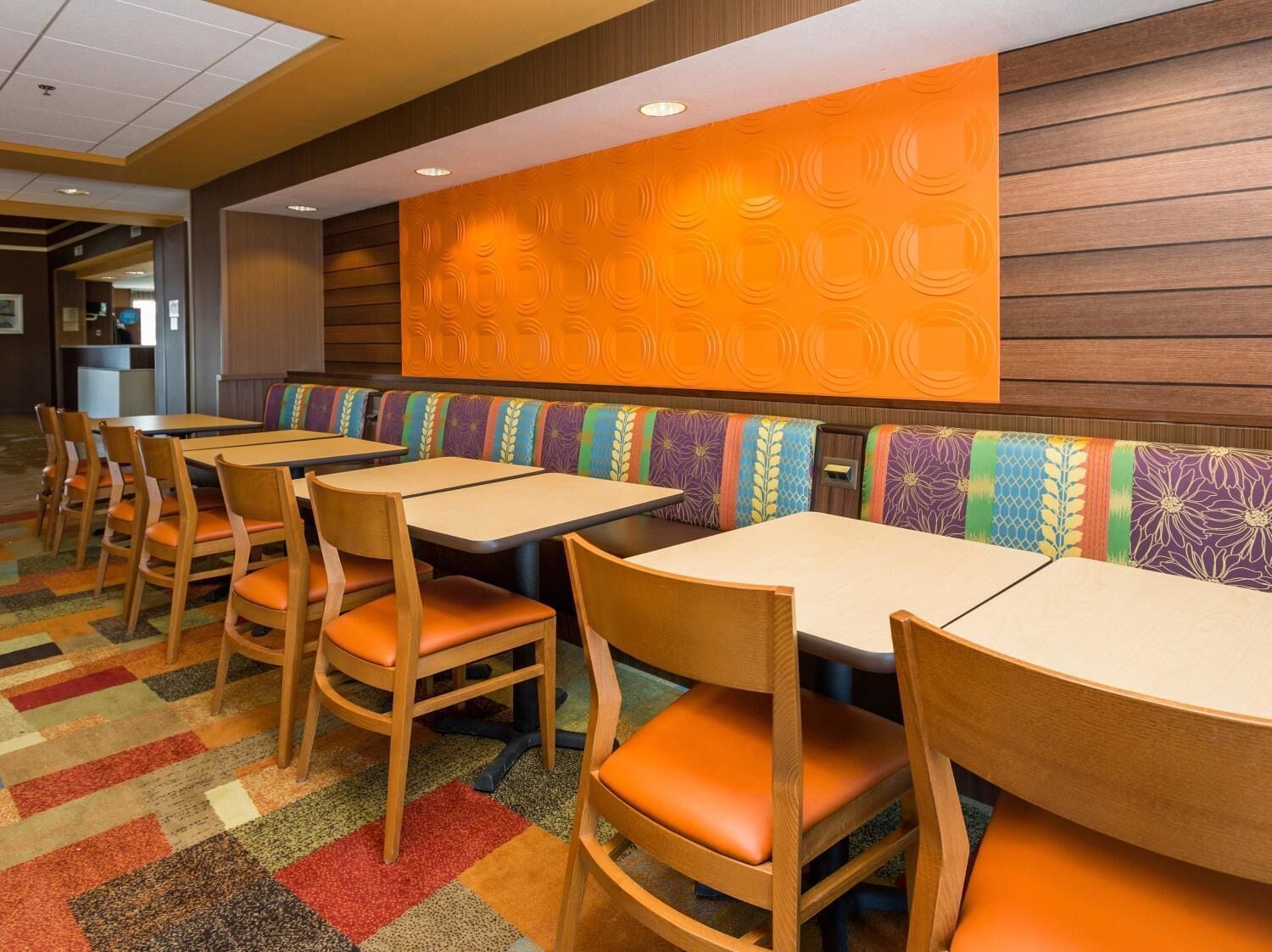 Un restaurante con mesas y sillas de madera, cómodos cojines con diseños coloridos y una pared estampada.