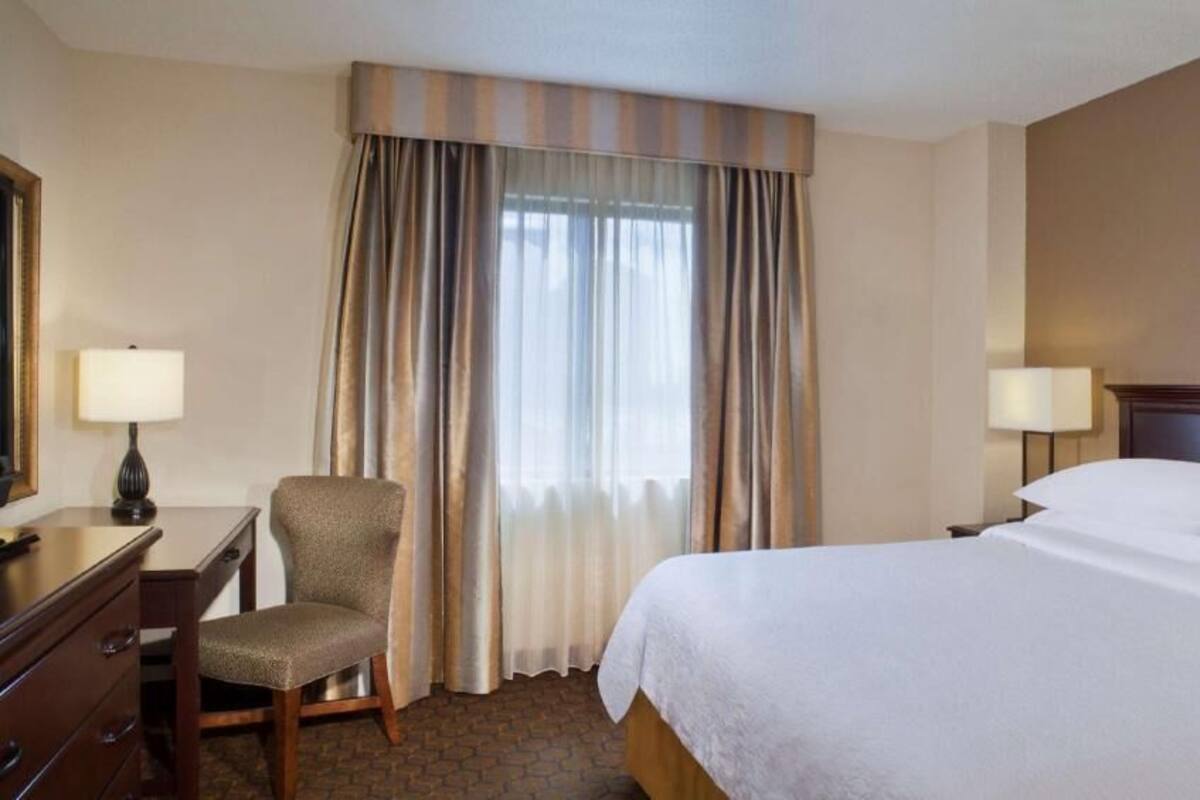 Une chambre d’hôtel avec un lit, un bureau, une chaise et des rideaux.