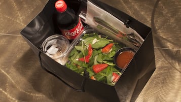 Uma sacola de presente preta contendo uma garrafa de Coca-Cola, um copo pequeno, uma salada com morangos e um recipiente com molho.