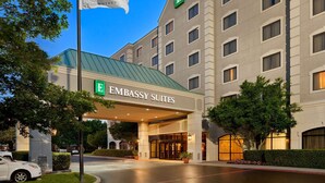 L’entrée d’un hôtel, avec une enseigne indiquant « EMBASSY SUITES » et un drapeau.