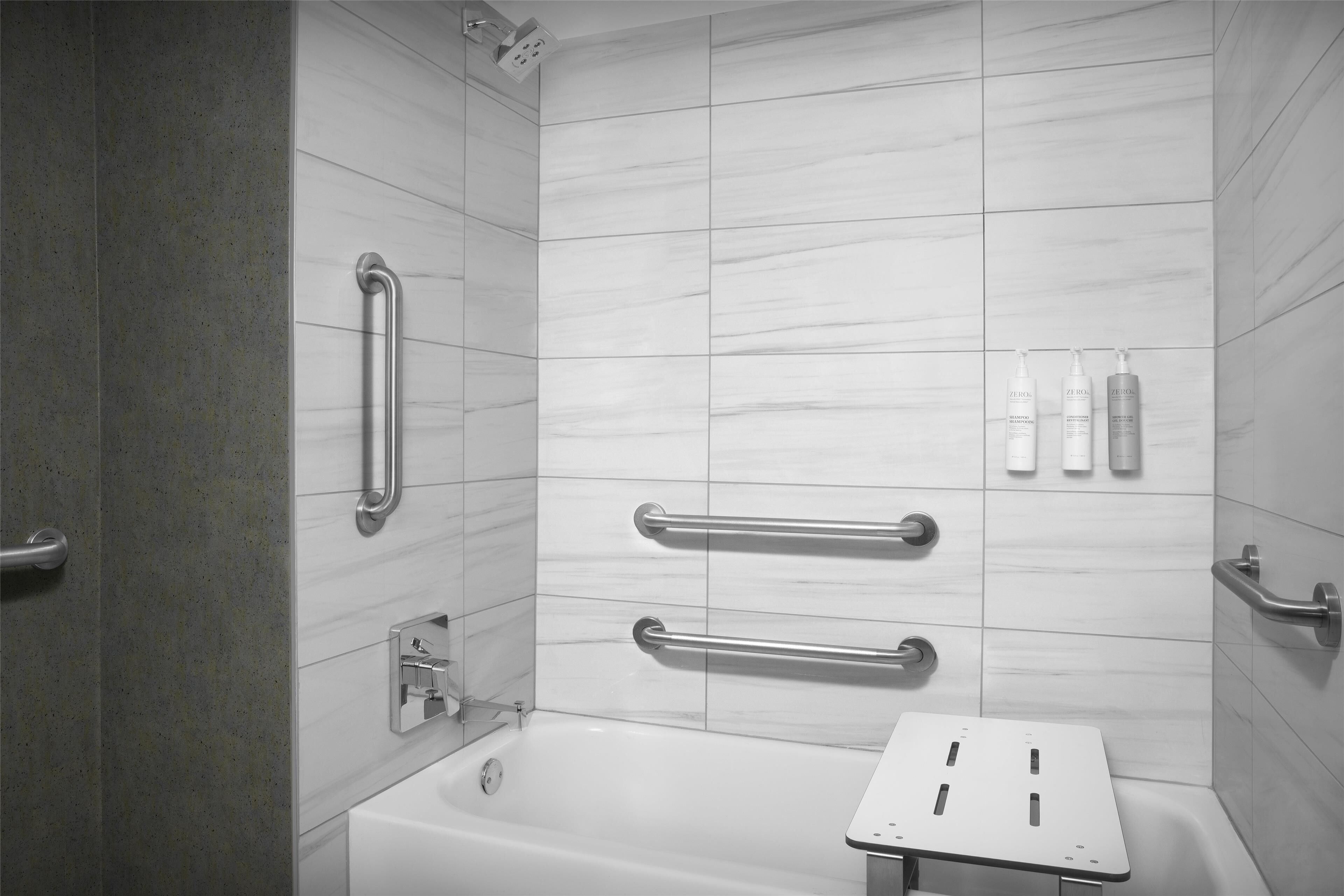 A modern bathroom with a bathtub, grab bars, and toiletries on the wall.