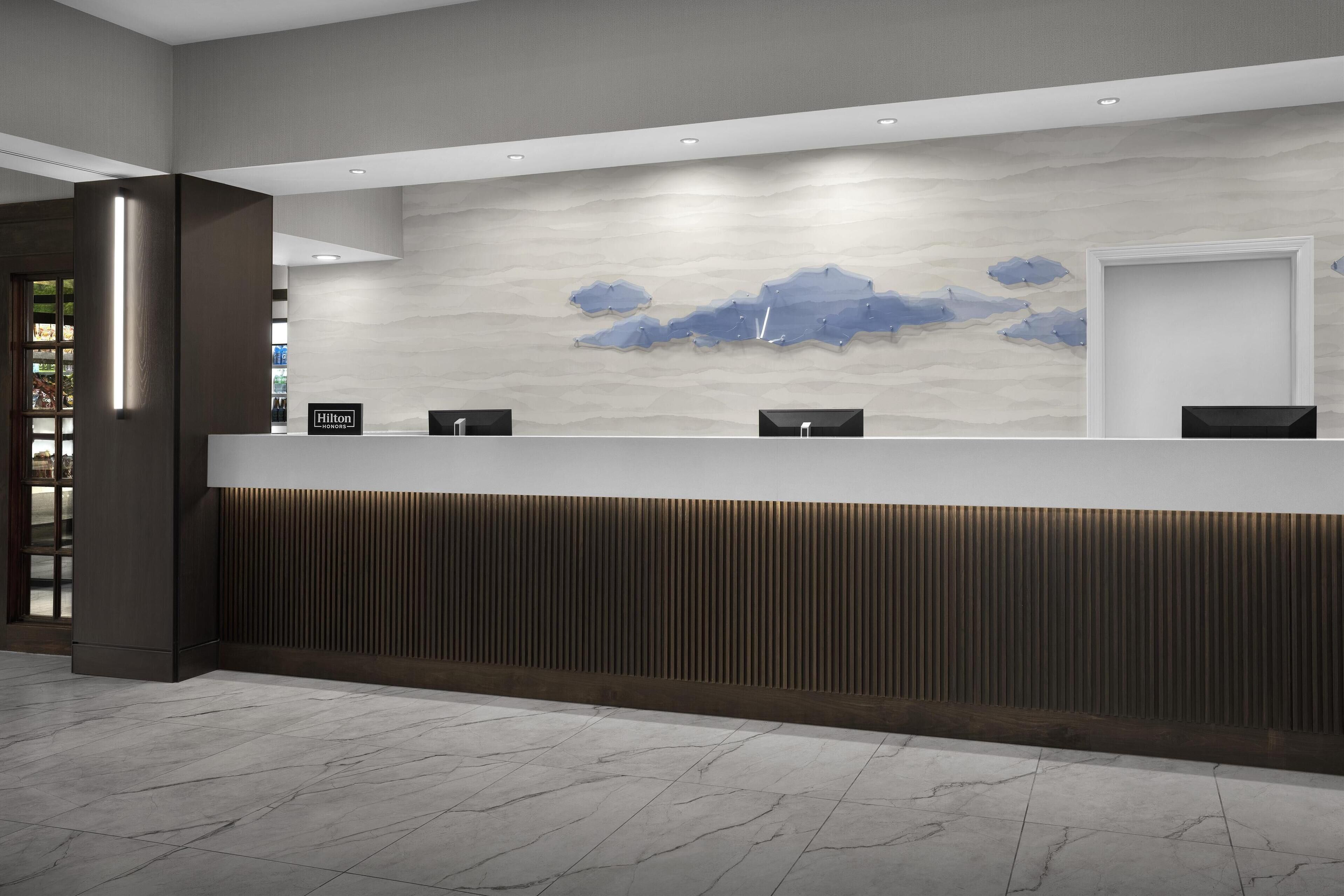 Un área de recepción de hotel moderna con suelo de mármol, un mostrador de madera y una pared con diseño que simula nubes.