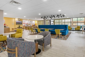 A modern lounge area with seating, a blue sofa, yellow chairs, and a dining area with tables and chairs. - Hampton Inn Richmond (Richmond)