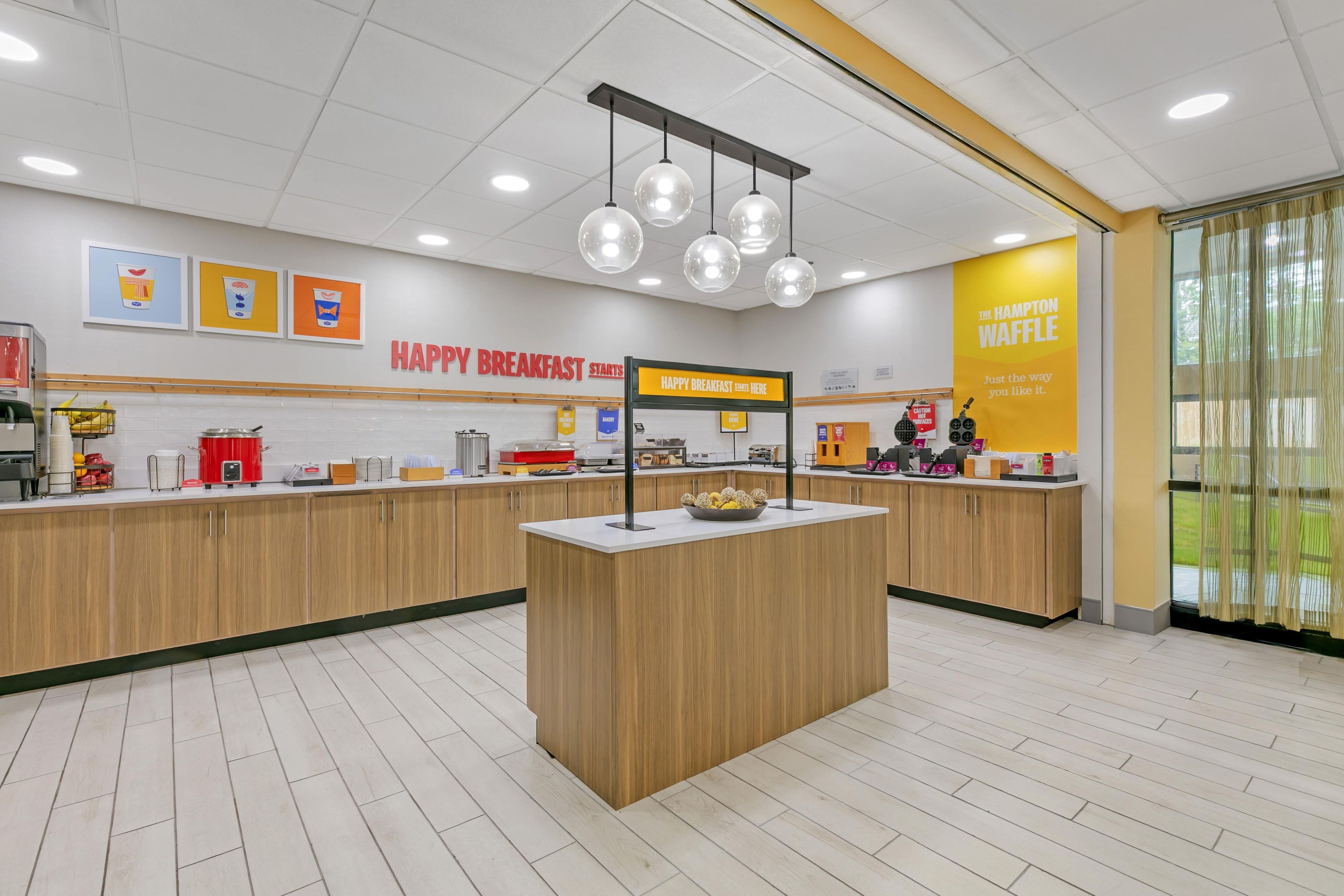 A clean, modern breakfast area with a central island, wooden cabinets, and a bright yellow wall with a sign.