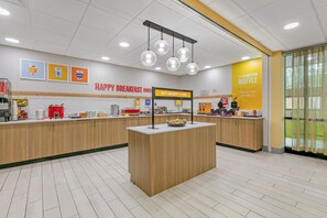 A clean, modern breakfast area with a central island, wooden cabinets, and a bright yellow wall with a sign. - Hampton Inn Richmond (Richmond)