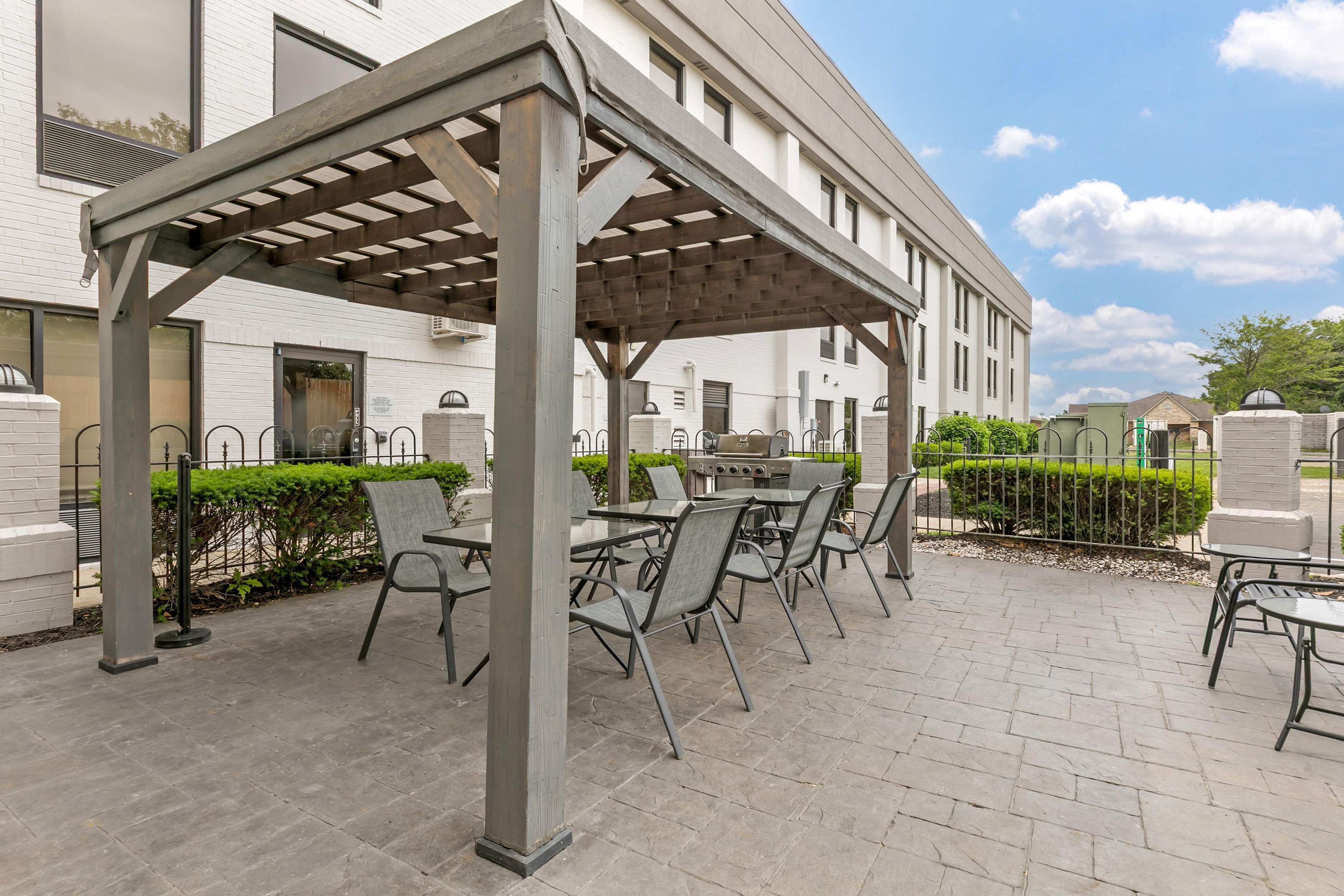 An outdoor patio with a pergola, seating, and a grill area.