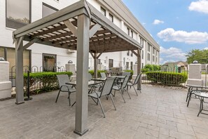 An outdoor patio with a pergola, seating, and a grill area.