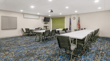 A conference room with a long table, chairs, a projector, flags, and a clock on the wall.