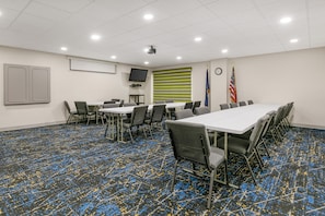 A conference room with a long table, chairs, a projector, flags, and a clock on the wall. - Hampton Inn Richmond (Richmond)
