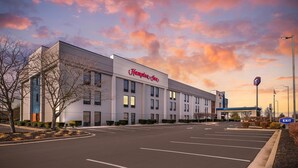 A Hampton Inn hotel with a parking lot and a clear sky with clouds.