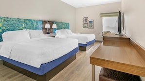 A hotel room with two beds, a desk, a TV, and artwork on the walls.
