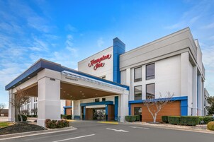 Um hotel Hampton Inn com entrada acessível, um posto de gasolina e um letreiro de 'Welcome'.