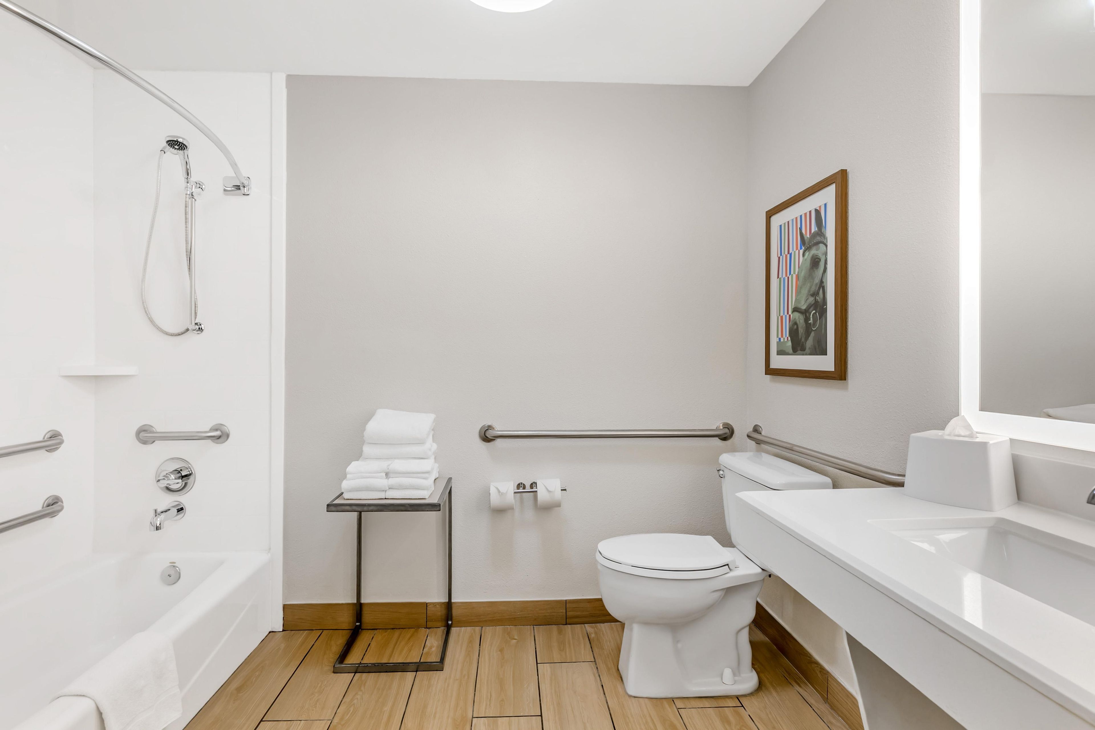 A modern bathroom with a bathtub, toilet, and sink, equipped with grab bars and a showerhead.