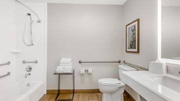 A modern bathroom with a bathtub, toilet, and sink, equipped with grab bars and a showerhead.
