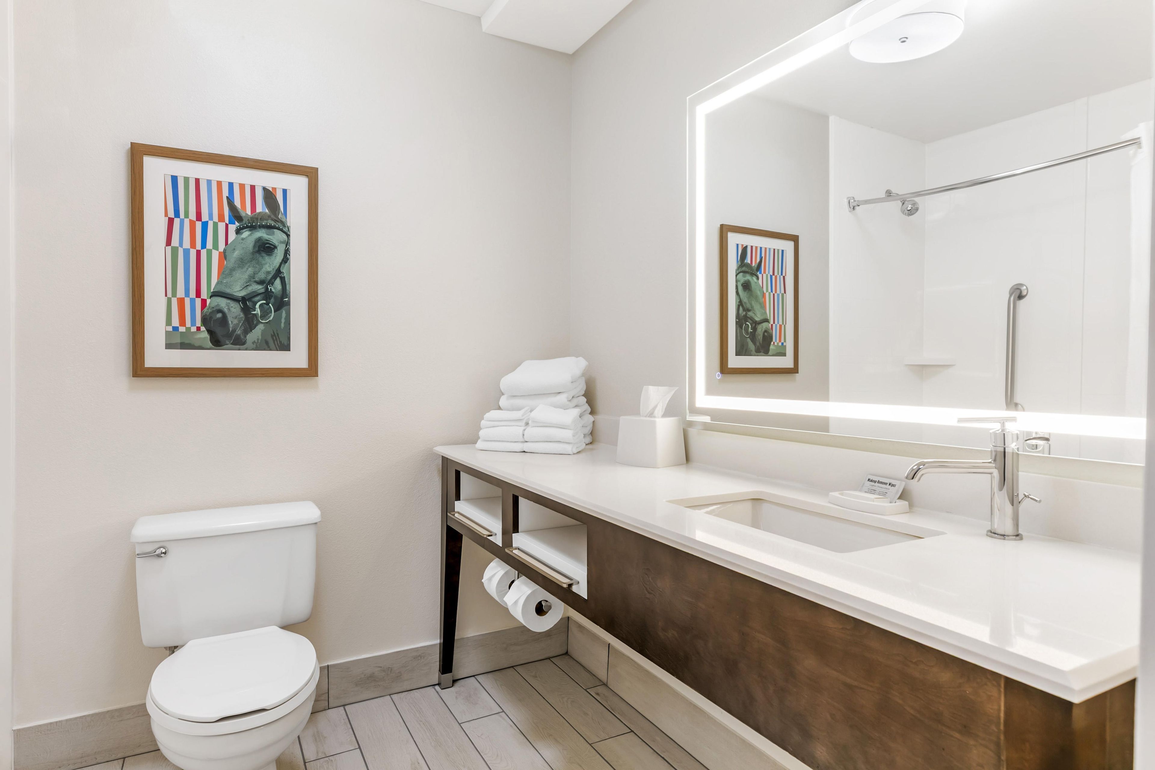 A modern bathroom with a toilet, sink, and shower. There are framed artworks on the walls.