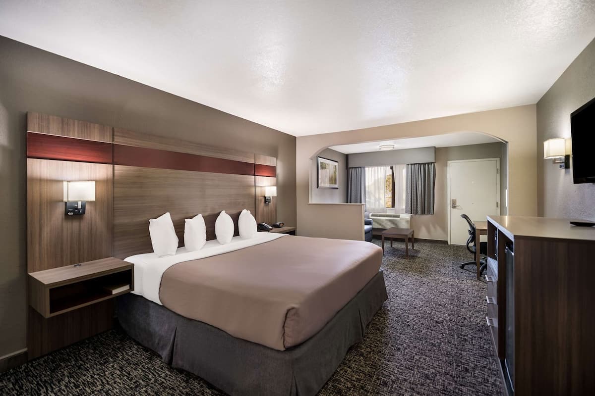 Ein Hotelzimmer mit einem großen Bett, Nachttischen, einem Schreibtisch, einem Sessel und einem Fernseher.