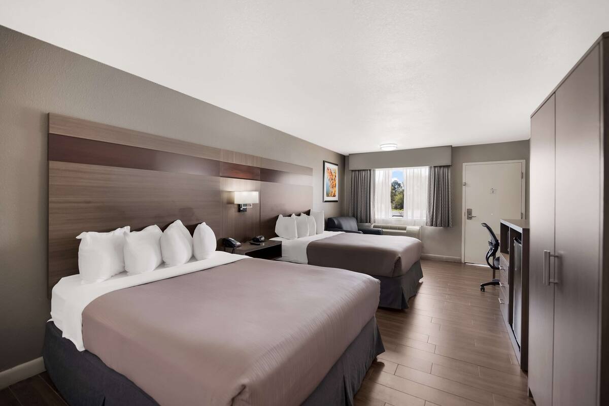 Ein Hotelzimmer mit zwei Betten, einem Schreibtisch, einem Sessel, einem Fernseher und einem Kleiderschrank.