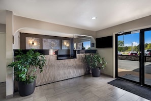 A reception area with a modern design, featuring a reception desk, potted plants, and a view of the parking lot through glass doors. - Best Western Minden Inn (Minden)